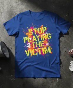 Royal blue t-shirt with yellow, orange, and pink paint splatter graphic and bold yellow text "STOP PLAYING THE VICTIM"