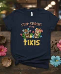 Stop Staring At My Tikis t-shirt design featuring two colorful tiki masks and tropical flowers