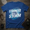 Stronger Than The Storm quote in bold white text on a blue t-shirt with abstract circular graphics and paint splatters