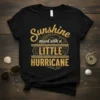 Black t-shirt with gold text reading "Sunshine mixed with a LITTLE HURRICANE" in a vintage distressed style, featuring sun and