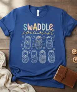 Swaddle Specialist quote with cute swaddled baby graphics on a blue t-shirt, perfect for new parents
