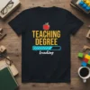 Teaching Degree Loading t-shirt with yellow text, loading bar graphic, and apple illustration