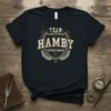 Team Hamby Lifetime Member text on a black t-shirt, featuring a shield emblem and laurel wreath