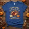 Thankful Grateful Blessed Happy Thanksgiving text with a geometric turkey graphic, pumpkins, and fall leaves on a blue t-shirt