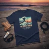 T-shirt with "THE PERFECT BREAK Ocean Harmony RIDE THE TIDE" text and a stylized surfing wave graphic at sunset