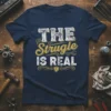 The Struggle Is Real quote in distressed white and gold typography on a navy t-shirt, with wrench graphic