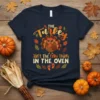 The Turkey Ain't The Only Thing IN THE OVEN graphic tee with a cute turkey and baby footprints, perfect for