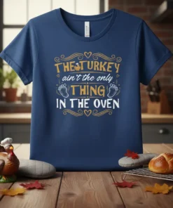 The Turkey Ain't The Only Thing In The Oven t-shirt design with gold and white text and baby feet graphics
