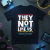 Bold white text reading "THEY NOT LIKE US" on a black t-shirt with geometric red, yellow, and blue accents