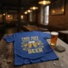 Blue t-shirt with "THIS GUY NEEDS A BEER BEER" text and graphics of hands holding beer mugs, hops, and barley