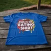 Blue t-shirt with "This Is My Eating Shirt" text in white, red, brown, and yellow, surrounded by colorful paint splatters
