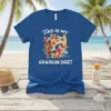 Blue t-shirt with white text "THIS IS MY HAWAIIAN SHIRT" above a vibrant floral graphic of a Hawaiian shirt, surfboard