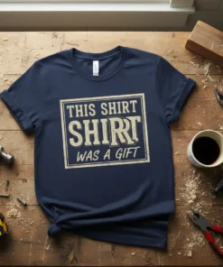 Navy blue t-shirt with distressed text reading "THIS SHIRT SHIRT WAS A GIFT" in a white box graphic