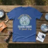 Blue t-shirt with "TRAINING HUMANS To Speak Dog" text, featuring a paw print and megaphone graphic