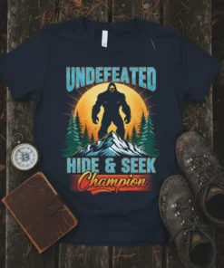 Undefeated Hide & Seek Champion Bigfoot t-shirt design with a silhouette of Bigfoot on a mountain peak against a large