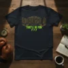 Black t-shirt with "Underestimate Me That'll Be Fun" text in distressed gold and neon green, featuring skull and wings graphics