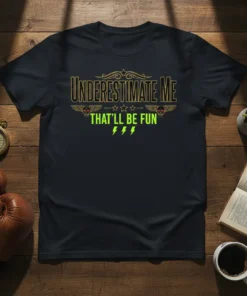 Black t-shirt with "Underestimate Me That'll Be Fun" text in distressed gold and neon green, featuring skull and wings graphics