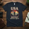 USA Bigfoot American Legend t-shirt design with Bigfoot holding an American flag and rock on hand