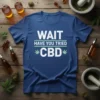 Blue t-shirt with white text "WAIT HAVE YOU TRIED CBD" and green accents, surrounded by CBD oil bottles and hemp