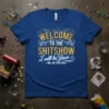 Welcome to the Shitshow I will be Your Host t-shirt with gold glittery text and white accents, on a royal