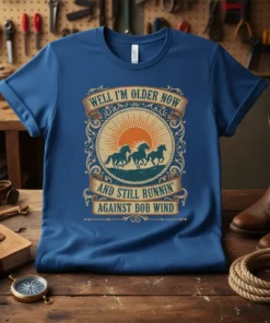 Graphic tee with vintage western design featuring running horses, sun, and the quote "Well I'm Older Now And Still Runnin'
