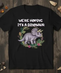 WE'RE HOPING IT'S A DINOSAUR text above a triceratops surrounded by floral wreath graphic on a black t-shirt