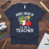 When I Grow Up I'll Be A Teacher quote with books, crayons, and apple on navy blue t-shirt