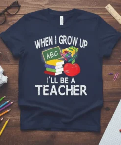 When I Grow Up I'll Be A Teacher quote with books, crayons, and apple on navy blue t-shirt