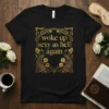 Black t-shirt with gold text "woke up sexy as hell again" and ornate peacock graphics