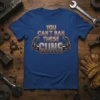 You Can't Ban These Guns text with muscular robot arms graphic on a blue t-shirt