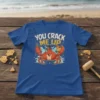 You Crack Me Up crab t-shirt design with a cartoon crab holding a chicken, funny seafood pun graphic