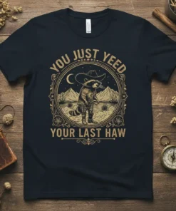 Graphic t-shirt with the phrase "YOU JUST YEED YOUR LAST HAW" and a raccoon wearing a cowboy hat and boots