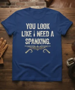 Bold white text "YOU LOOK LIKE I NEED A SPANKING." on a blue t-shirt with decorative golden whips below